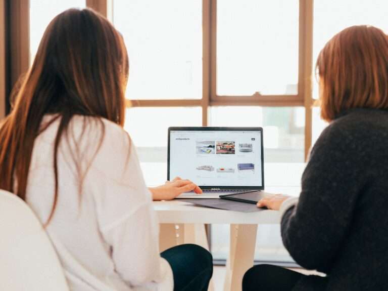 two women talking while looking at laptop computer