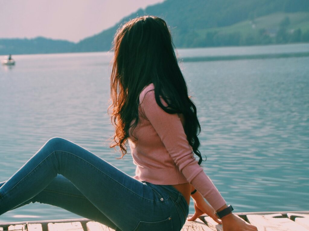 woman sitting on beach dock while looking on boat